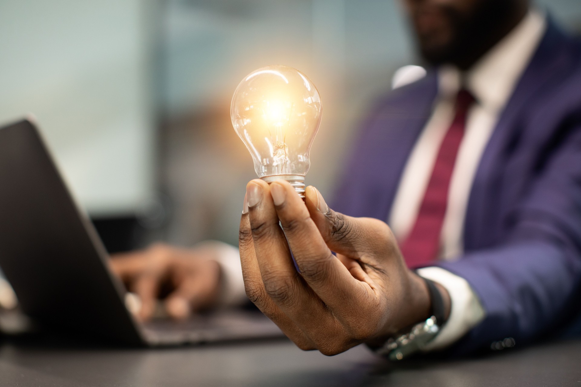 Black businessman holding illuminated light bulb, sitting in office